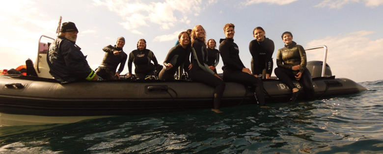 A group of scuba divers in wetsuits poses for the camera on an inflatable boat in the water